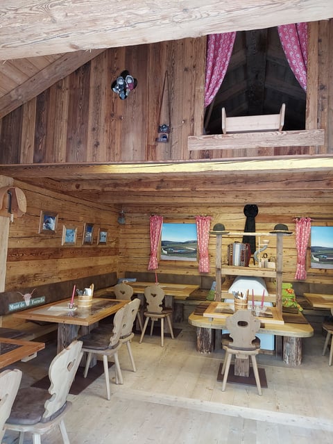 Cozy wooden loft interior with rustic dining tables, white chairs, pink curtains, and large windows with mountain views