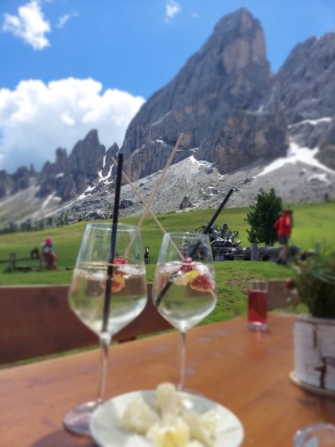 Wine glasses with mountain views at an outdoor Alpine restaurant overlooking dramatic rocky peaks and green meadows