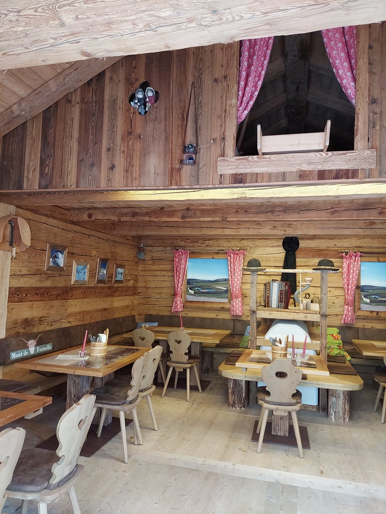Rustic wooden cabin interior with dining tables, chairs, and pink curtains on windows overlooking mountains