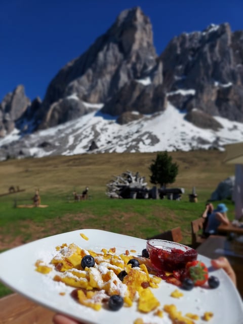 Plate of waffles with berries and jam in foreground with dramatic snow-capped mountain peaks and meadow in background