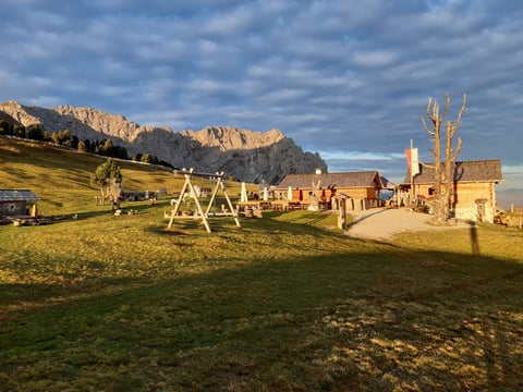 Alpine village with wooden swing set and historic buildings beneath dramatic mountain peaks under cloudy sky