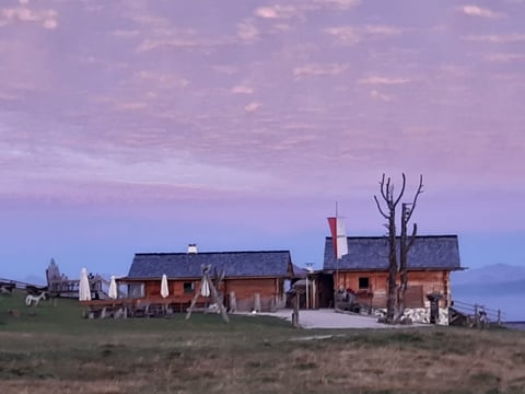 Red brick farmhouse with outbuildings on grassy prairie under purple twilight sky at dusk